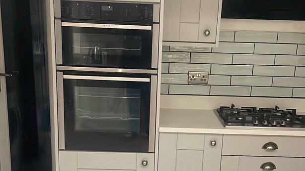 Een keuken met twee ovens, een gasfornuis en witte keukenkastjes.