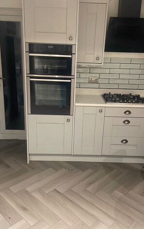 Una cocina con dos hornos, estufa a gas y armarios blancos.