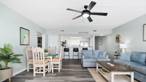 Ein modernes Wohnzimmer mit Essbereich, einer Küche im Hintergrund und einem Deckenventilator.