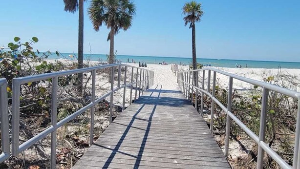 A wooden boardwalk leading to a beach with palm trees and a clear blue sky.