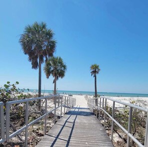 A wooden boardwalk leading to a beach with palm trees and a clear blue sky. - π΄ Coastal Escape at Madeira Bay Resort #310 β Stunning Marina Views & Steps from the Sand! π (Madeira Beach)