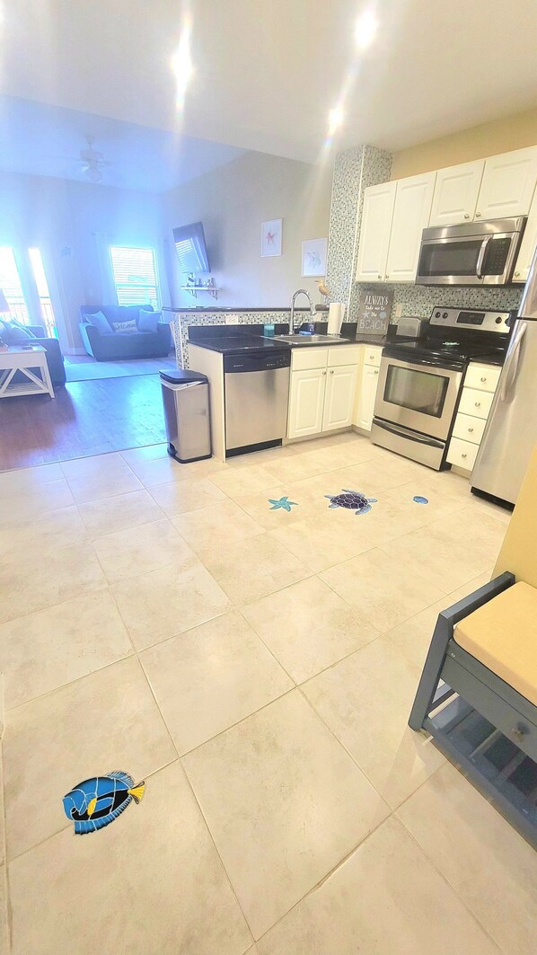 A spacious kitchen with modern appliances, a dining area with a sofa, and a view of the living room. - π΄ Coastal Escape at Madeira Bay Resort #310 β Stunning Marina Views & Steps from the Sand! π (Madeira Beach)