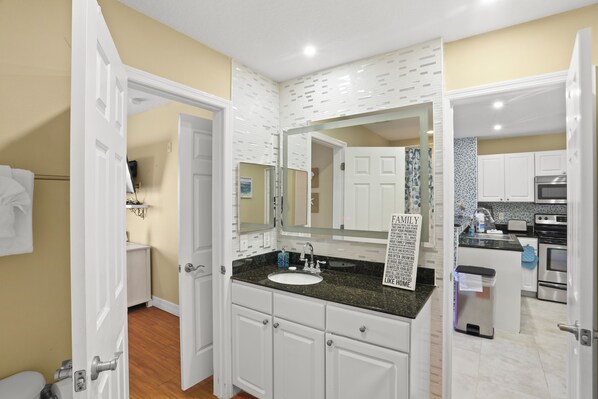 Un baño moderno con muebles blancos, encimera de granito y un espejo grande.