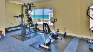 A gym with exercise equipment, a large mirror, and a view of the ocean through the windows.