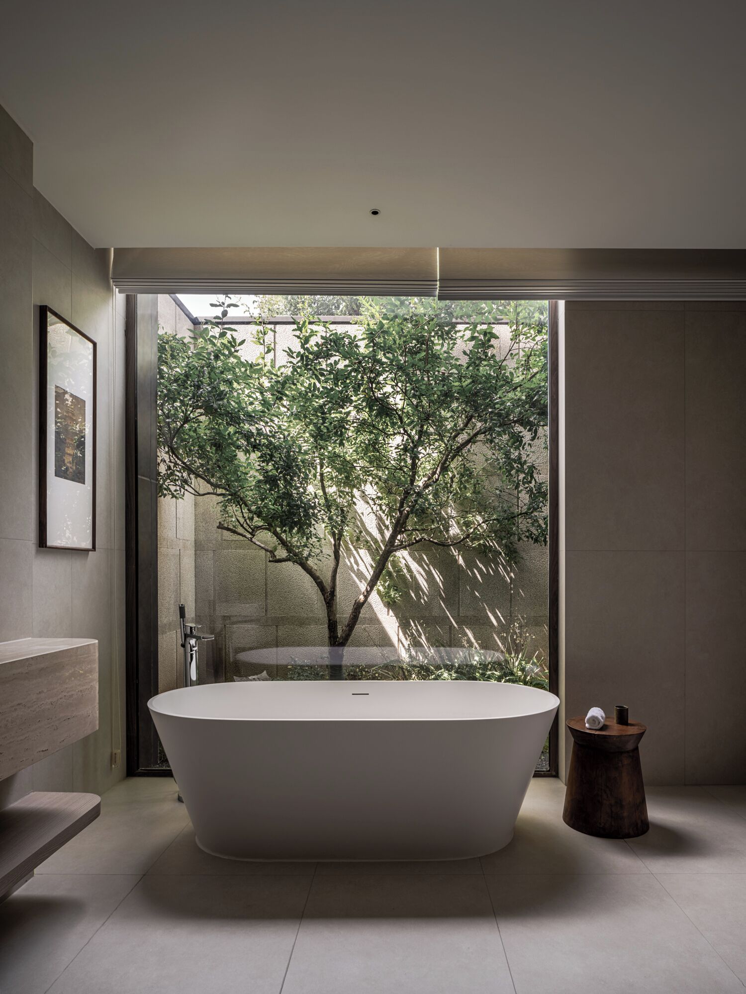 Un baño moderno con una bañera independiente, un box de ducha de cristal y vista a un árbol a través de la puerta de cristal.