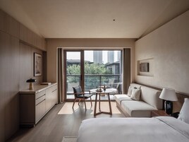 Ein modernes Hotelzimmer mit einem großen Bett, einer Couch, einem Esstisch und einem Balkon mit Blick auf die Stadt.