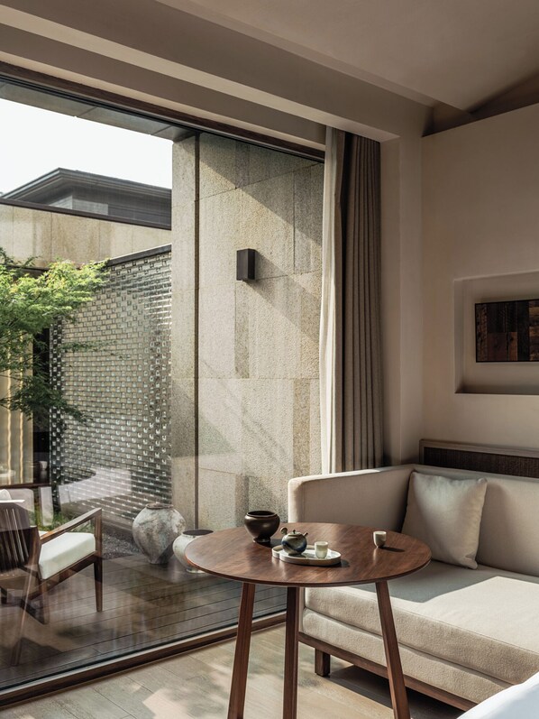A modern living room with a sofa, a round wooden table, and a glass partition. - Younch Hotel Xi'An (Xi'an)
