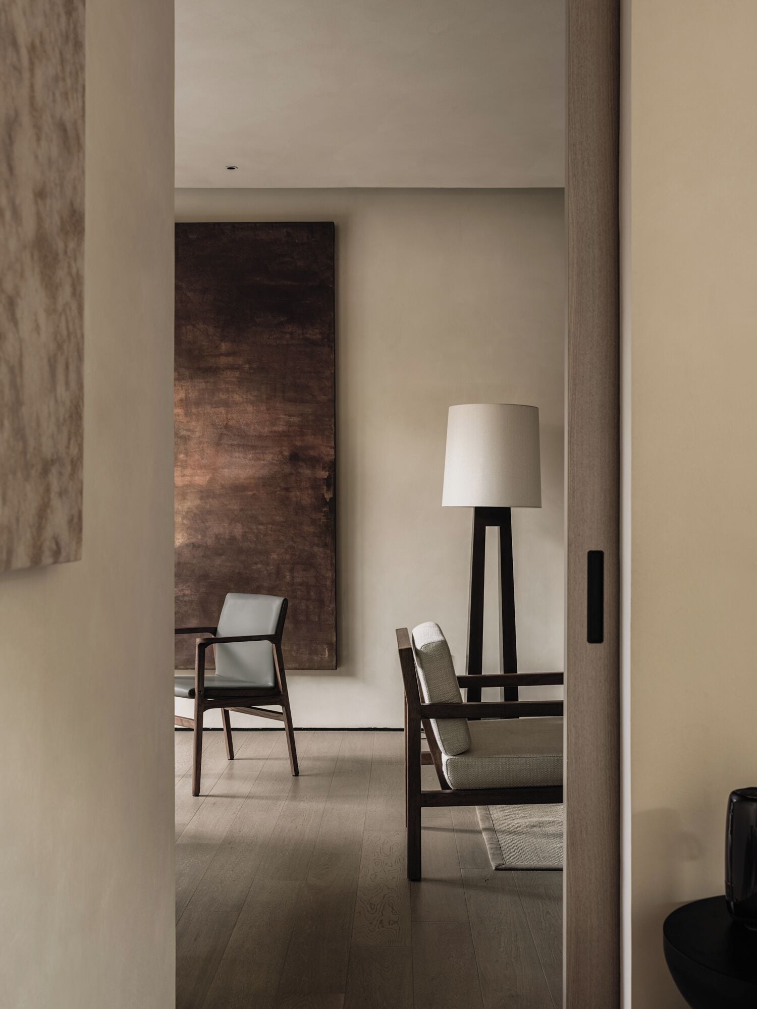 Una habitación moderna con diseño minimalista, que incluye dos sillas, un cuadro abstracto grande y una lámpara de pie.