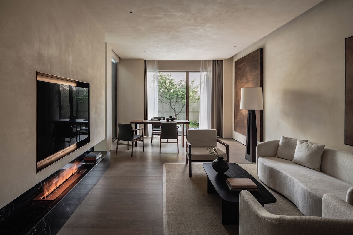 Una habitación de hotel moderna con televisor de pantalla plana, chimenea, zona de comedor con mesa y sillas, y sofá.