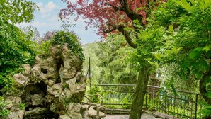 Ein Garten mit Felsformation, Steinbank und Metallzaun.