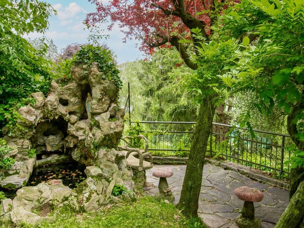 A garden with a rock formation, a stone bench, and a metal fence.