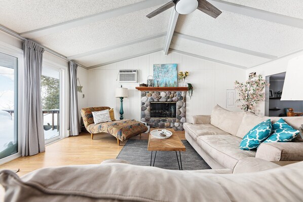 A cozy living room with a stone fireplace, a sofa, a coffee table, and a patterned armchair. - Lakeshore Lux - La Casa | Beach | Fireplace | AC (Williamsburg)
