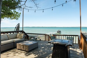 A wooden deck with outdoor furniture, a view of the sea, and a boat in the background. - Lakeshore Lux - La Casa | Beach | Fireplace | AC (Williamsburg)