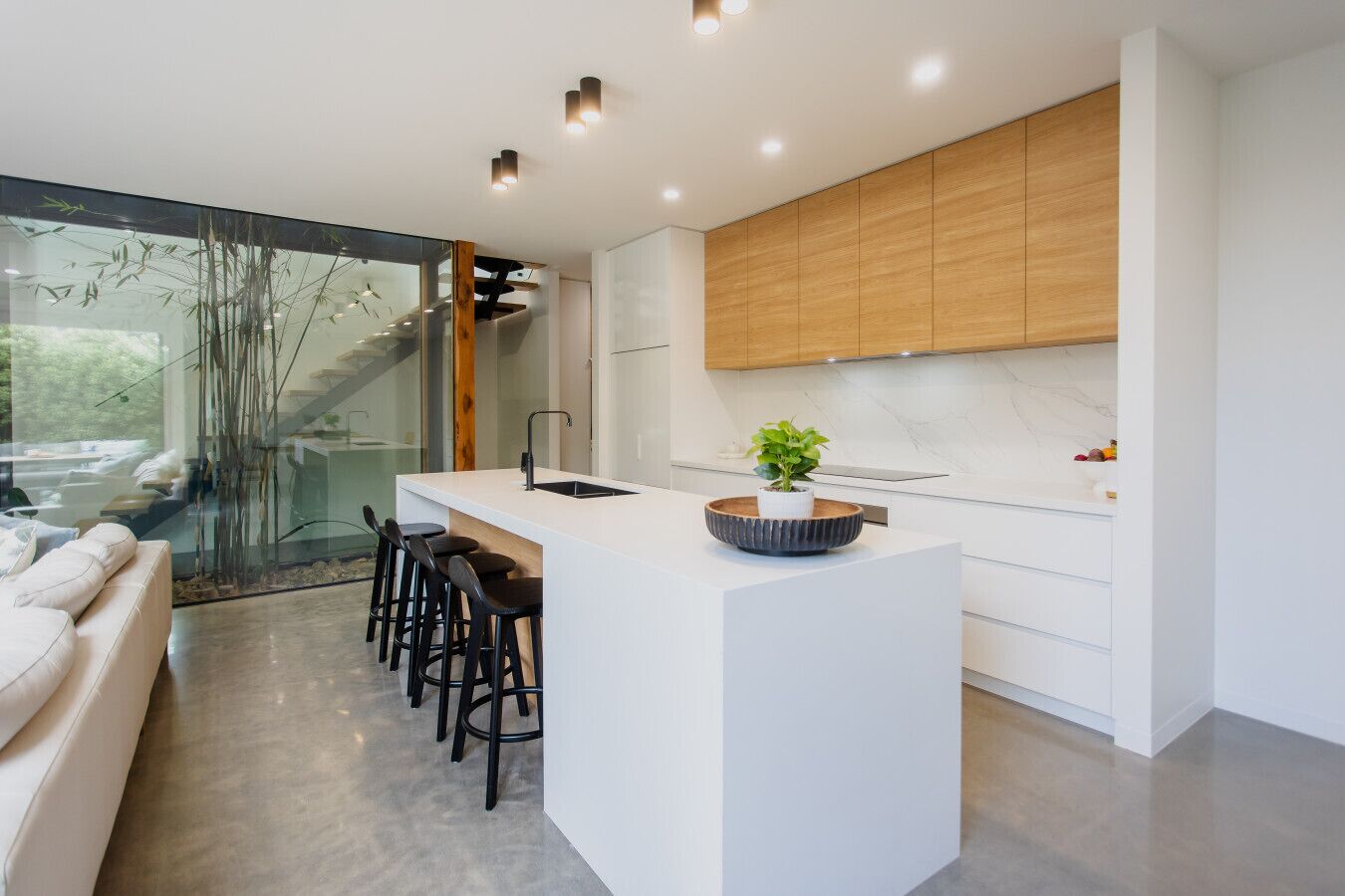 A modern kitchen with a central island, bar stools, and a large window overlooking a garden.