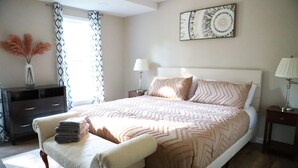 A bedroom with a bed, bedside tables, a dresser, a bench, and a wall art piece.