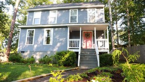 A two-story house with a front porch, a red door, and a small garden area with various plants and flowers.