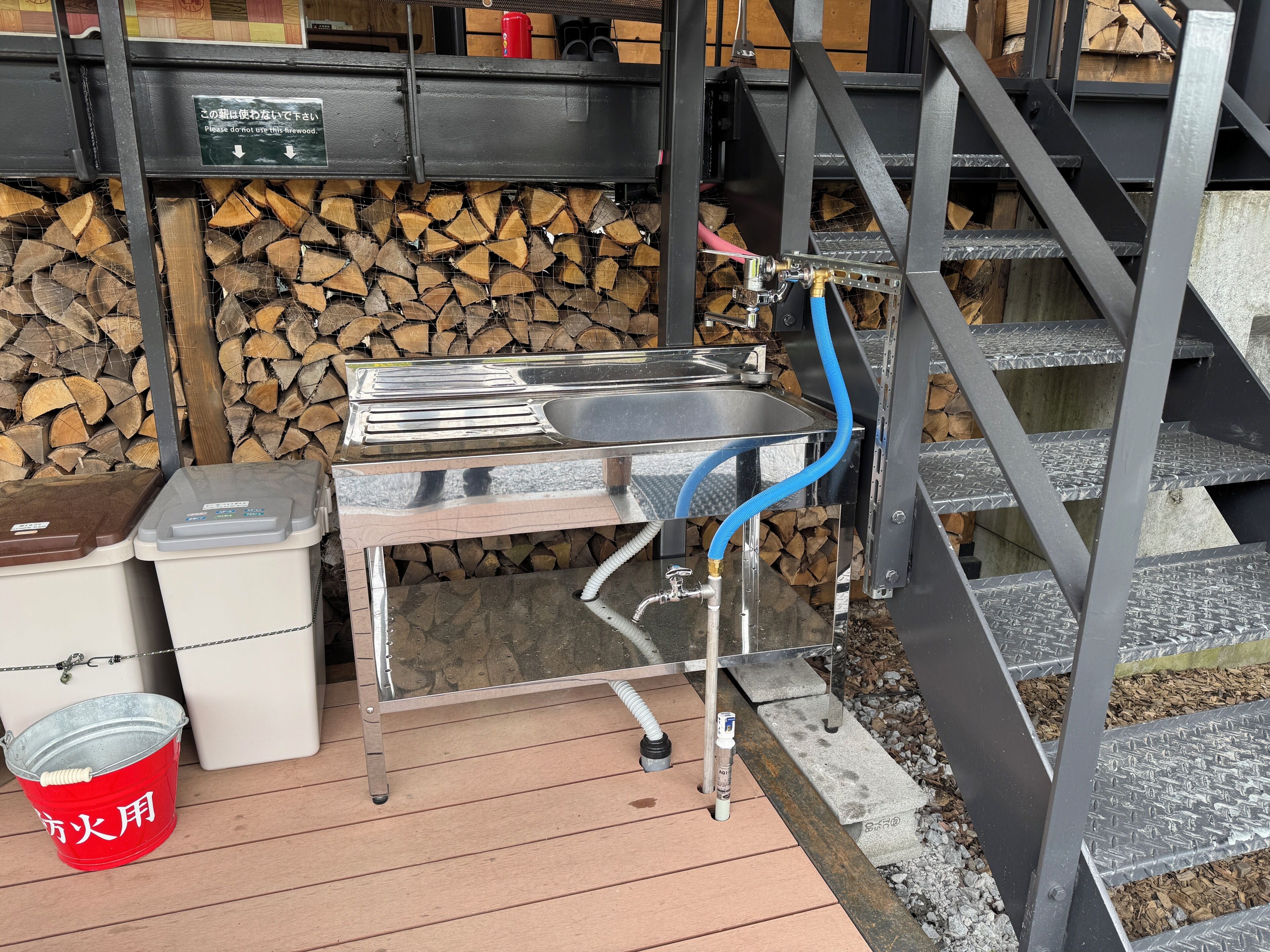 A metal table with a sink, a red bucket, and a hose.