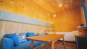 A cozy room with a wooden ceiling, a blue sofa with patterned cushions, a small wooden table, and a bed with white bedding. - SAUNA&Villa takibi (Makkari-mura)