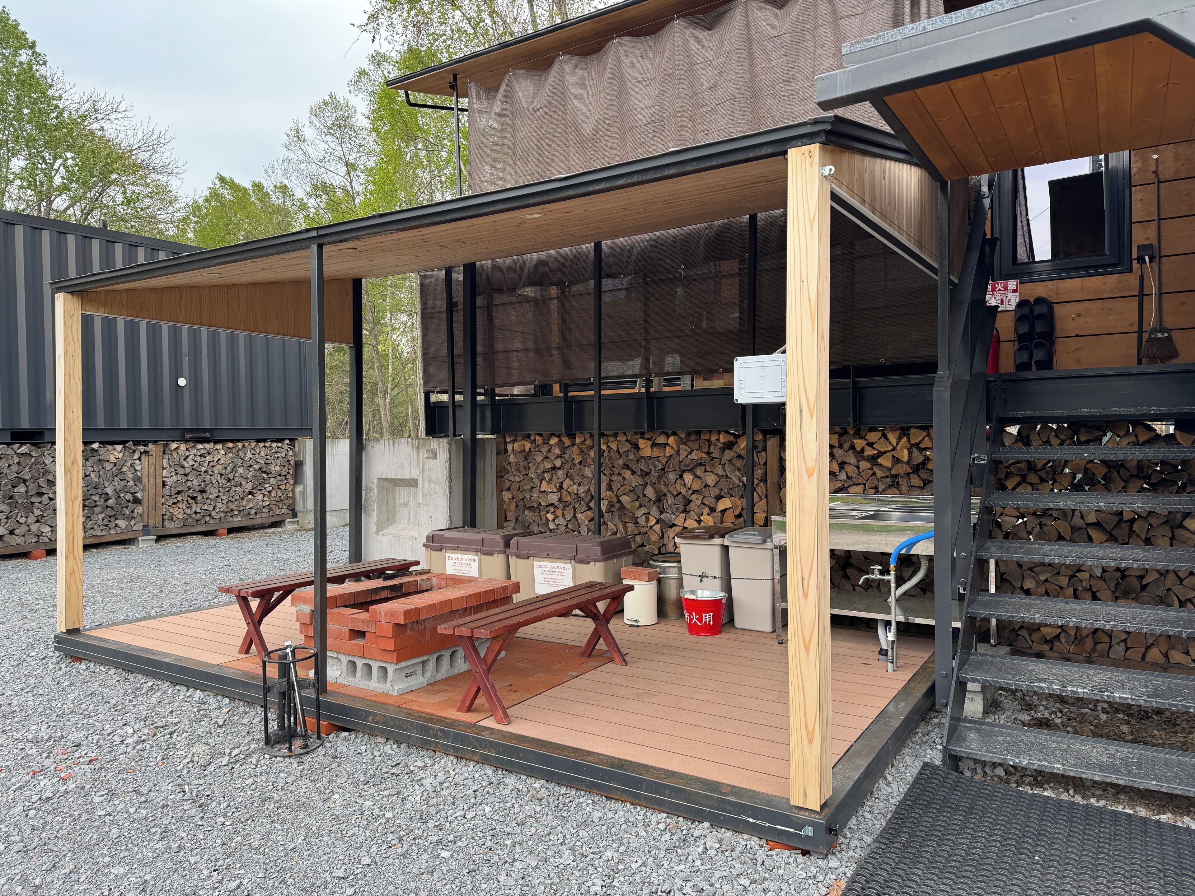 Een overdekt terras buiten met picknicktafels, een barbecue en een vuurplaats.