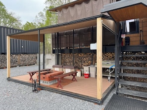 An outdoor covered patio with picnic tables, a grill, and a fire pit area.