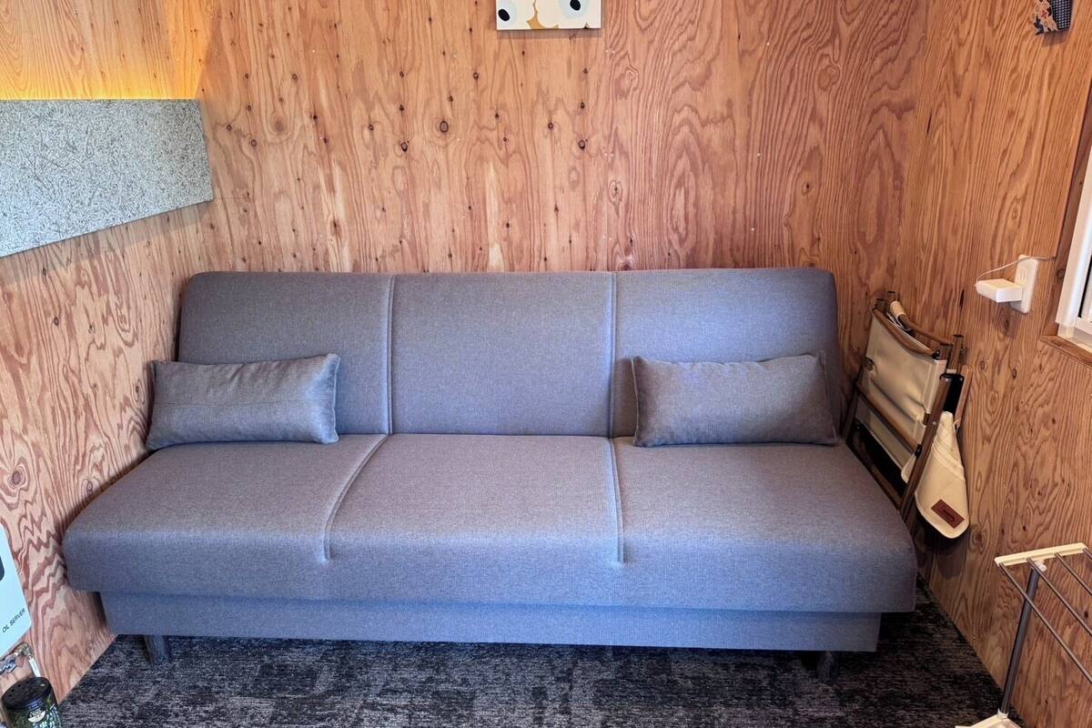 A grey sofa with two cushions against a wooden wall.
