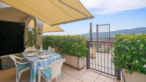 An outdoor patio with a table set for two, surrounded by potted plants, under a canopy.