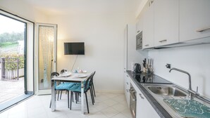 A modern kitchen with a dining area, a TV mounted on the wall, and a sliding glass door leading to an outdoor area.