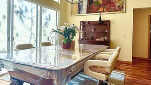 Un coin repas comprenant une table avec un plateau en verre, des chaises, une plante en pot et un meuble en bois.
