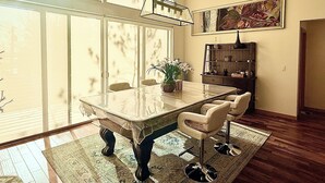 Un coin repas avec une table à plateau en verre, quatre chaises, un vase avec des fleurs, une bibliothèque et un tableau accroché au mur.