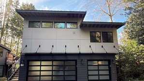 Une maison moderne à deux étages, dotée d’un garage, de grandes fenêtres et d’un toit plat.