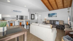 A modern kitchen with white cabinets, a wooden ceiling, and a sign that reads "MERMAIDS".