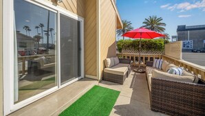 A patio with wicker furniture, a red umbrella, and a view of palm trees.