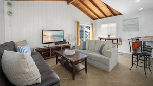 A living room with a wooden ceiling, a television, a sofa, a coffee table, and a dining area with chairs and a table.
