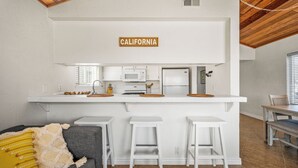 A compact kitchen with white cabinetry, a microwave, and a refrigerator. A sign above the counter reads "CALIFORNIA". - Cozy Beach Duplex Steps to Sand and Shops (Newport Beach)