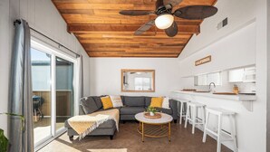 A modern kitchen with white cabinets and a countertop, a gray sofa with yellow cushions, and a ceiling fan. - Cozy Beach Duplex Steps to Sand and Shops (Newport Beach)