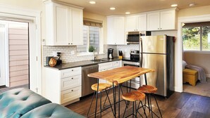Una cocina moderna con armarios blancos, electrodomésticos de acero inoxidable y una zona con taburetes de madera.