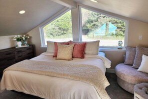 A bedroom with a large bed, two windows, a dresser, and a chair. - Ocean View! Charming Home with Loft, Sleeps 6! Dog Friendly! (Yachats)