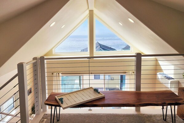 Ein Zimmer mit hohen Decken und einer geneigten Decke, mit großem Fenster mit Blick auf ein Gewässer.