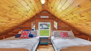 Ein gemütliches Schlafzimmer im Dachgeschoss mit zwei Betten, einer Holzbalkendecke und Blick ins Freie.