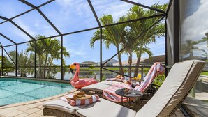 A poolside area with lounge chairs, a flamingo float, and a table with a drink and snacks.