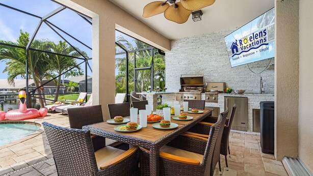 An outdoor dining area with a pool, wicker chairs, and a grill.