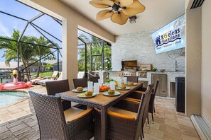 An outdoor dining area with wicker chairs and a poolside view. - Heated Pool, Gulf Access, Dock, Outdoor Kitchen - Gulf Coast Haven - Roelens (Cape Coral)