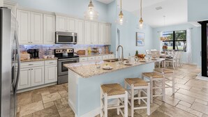 A kitchen with white cabinets, a granite countertop, a central island with bar stools, and pendant lighting.