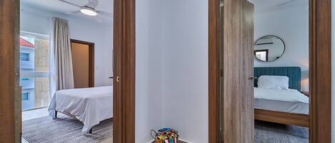 A hotel room with a bed, a ceiling fan, a mirror, and a view of the outside.