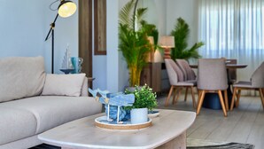 Una sala de estar moderna con un sofá, una mesa de centro con adornos, una lámpara y un comedor con sillas y una mesa.