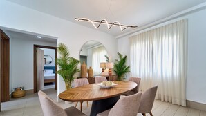 Un comedor moderno con una mesa redonda de madera rodeada por seis sillas, una lámpara contemporánea arriba y grandes ventanas con cortinas.