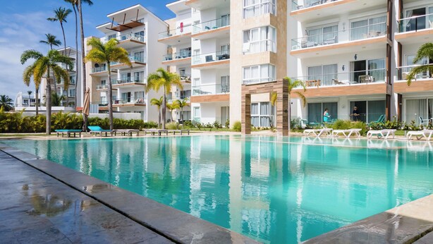 Un hotel moderno con una piscina grande, palmeras y varios balcones.