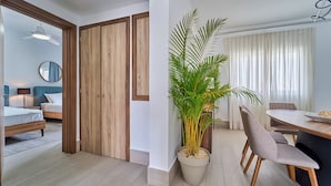 Una habitación de hotel moderna con un armario de madera, un espejo redondo, una cama, una mesa de comedor con sillas y una planta grande en maceta.