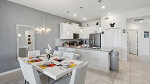 A modern kitchen with white cabinets, a central island, and a dining area with a white table and chairs.