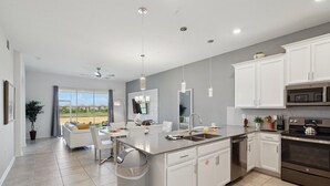A modern kitchen with white cabinetry, a large island, stainless steel appliances, and a view to the outside.